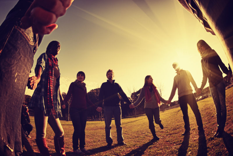 a group of millennials standing in a circle holding hands with bright sunlight in background