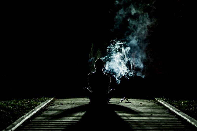 silhouette of man meditating on dark path surrounded by smoke